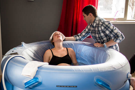 Woman laboring in birth pool with husband touching forehead